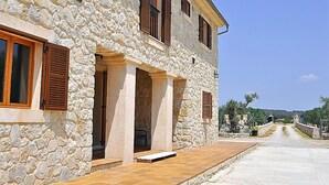 A stone building with wooden shutters, a paved entrance, and a view of the countryside.
