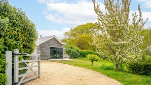 A house with a gravel driveway, a wooden gate, and a garden with blooming trees. - Peterstone Lodge, Holkham, Norfolk (Wells-next-the-Sea)