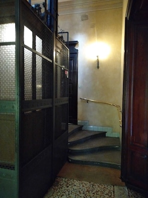 Stairwell with a metal railing and a wooden door, featuring a patterned rug and a light fixture.