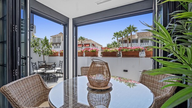A glass-enclosed patio with wicker furniture, a round glass table, and a decorative wicker centerpiece.