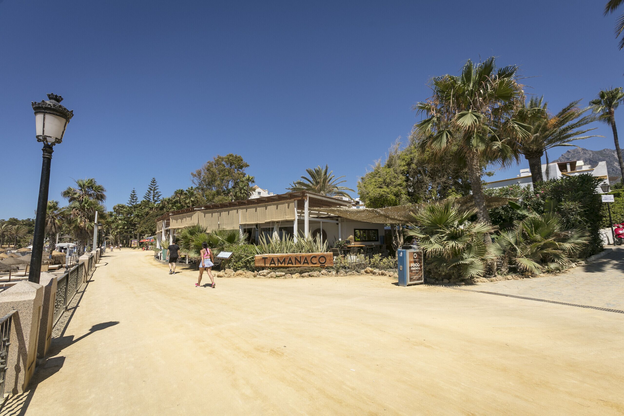 A Tamanaco restaurant with a sign, palm trees, and a clear blue sky.