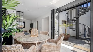 A modern living room with wicker furniture, a glass table, and a large potted plant.