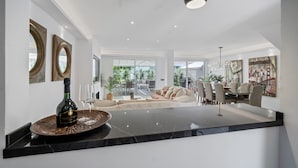 A modern kitchen with a marble countertop, a wine bottle, and glasses. There is a dining area with a round table and chairs.