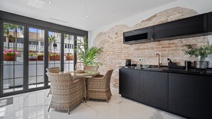 A modern kitchen with a brick wall, black cabinets, and a large window overlooking a courtyard with plants.