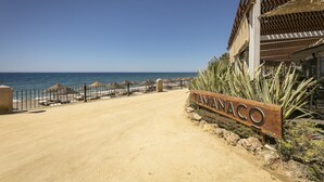 A beachside entrance with a sign reading "TAMANACO," a sandy path, and a view of the ocean.