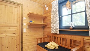 Interior de una cabaña de madera con un banco, una ventana con cortinas y una repisa con tazas.