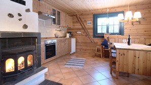 Interior de una cabaña de madera con chimenea de piedra, armarios de madera, una mesa de comedor y una ventana con vistas.