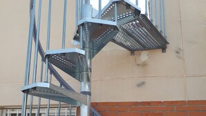 A spiral staircase with metal railings, leading to a window with a metal grille.