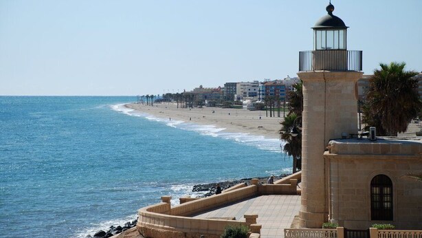 A coastal view with a lighthouse, beach, and buildings in the background.