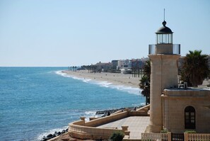 Vista costeira com farol, praia e edifícios ao fundo.