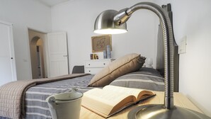 Un lit bien fait, recouvert d’une couverture à rayures, une lampe de chevet, un livre et une tasse posés sur une table de chevet en bois.