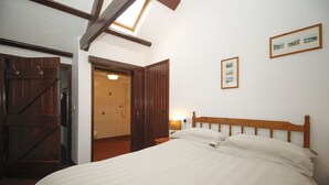 A bedroom with a large bed, wooden headboard, a skylight, a wooden wardrobe, and a framed picture on the wall. - 2 bedroom cottage on Bodmin Moor (Bodmin)