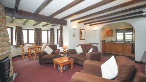 A cozy living room with a fireplace, a dining area, and a kitchen visible through an archway. - 2 bedroom cottage on Bodmin Moor (Bodmin)