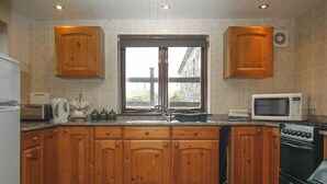 A kitchen with wooden cabinets, a window, a microwave, and a stove. - 2 bedroom cottage on Bodmin Moor (Bodmin)