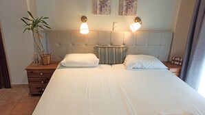 A neatly made bed with white linens, two bedside lamps, a striped pillow, a small table with a plant, and a book on the bed. - Floor apartment with superb roof terrace, next to Almirida sandy beach   (Chania)