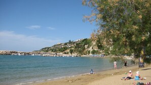 A beach with clear blue water, a rocky shoreline, and a few people relaxing. - Floor apartment with superb roof terrace, next to Almirida sandy beach   (Chania)
