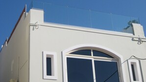 A building with a white facade, a large arched window, and a flat roof with a visible antenna. - Floor apartment with superb roof terrace, next to Almirida sandy beach   (Chania)