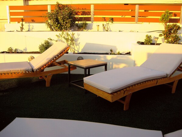 A patio with wooden lounge chairs and a small table.