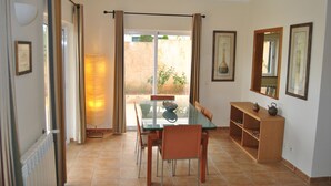 A dining area with a glass table and chairs, a wooden sideboard, and a view through a glass door to an outdoor area.