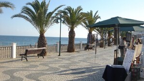 A paved promenade with benches, palm trees, and a market stall with artwork.