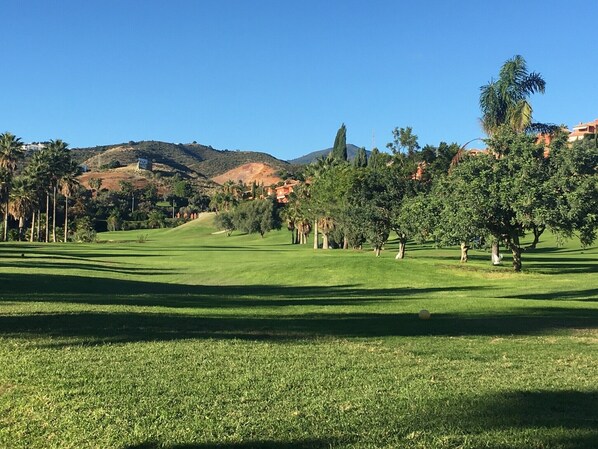 Ein Golfplatz mit freiem Blick auf das Grün, Bäume und die entfernten Hügel.