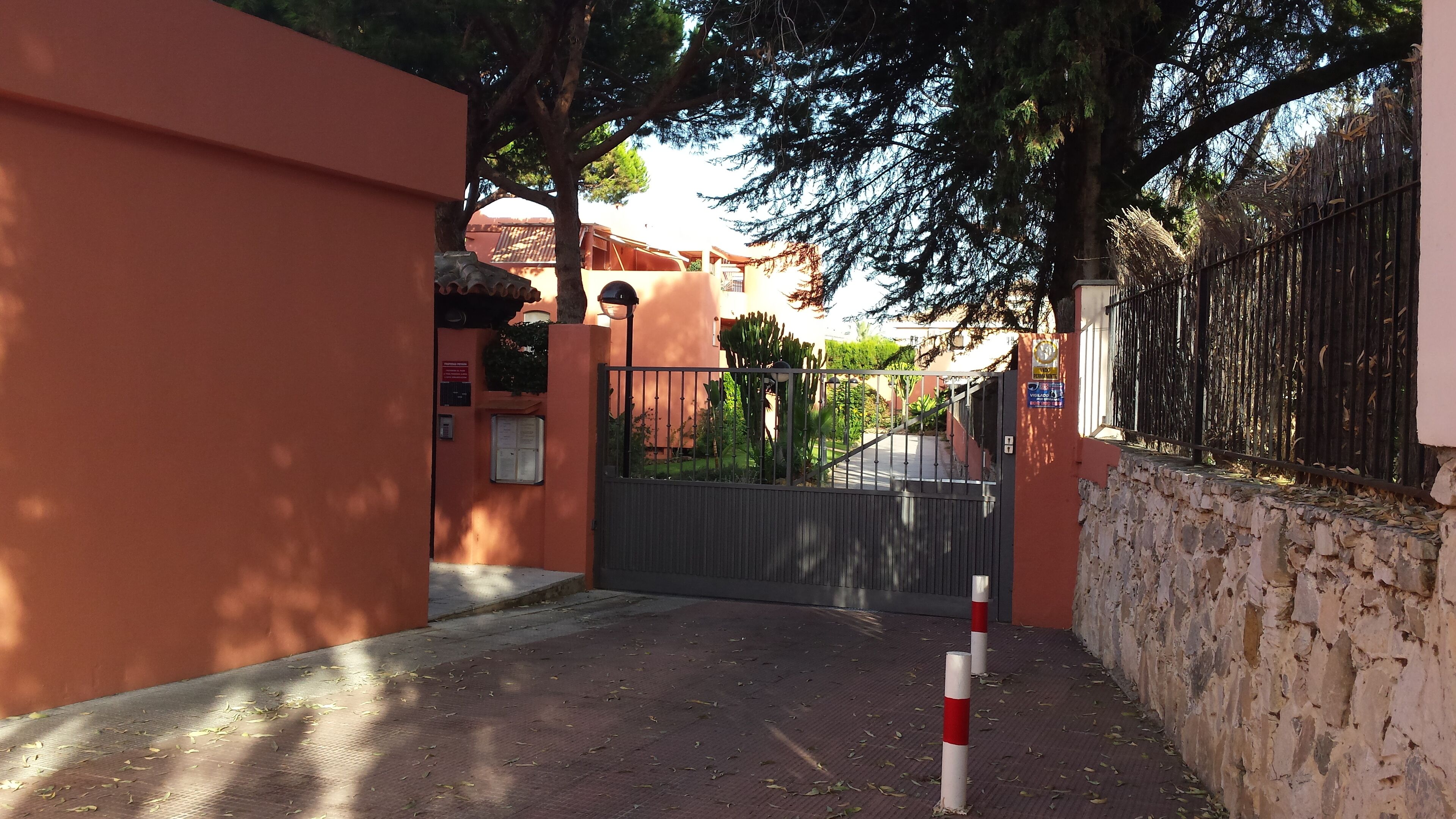 A gated entrance with a metal gate, a stone wall, and a tree-lined path.