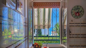 A kitchen with a view through a window, a clock, and a fruit bowl with a drink. - House / Villa - Sciacca (Sciacca)
