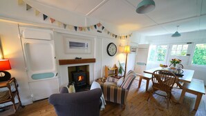 A cozy living room with a fireplace, wooden furniture, and a dining area. - Charming Seaside Home, Full of Character (Old railway carriages) Pet Friendly,  (Chichester)