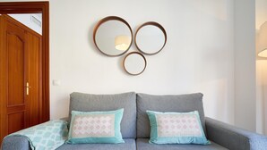 Un sofá gris con cojines estampados, una puerta de madera y espejos circulares colgados en la pared.