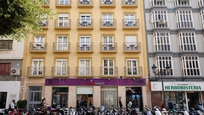 Un edificio de varios pisos con balcones, una tienda llamada 'ClaraVision' y una 'La Central HERBORISTERIA' al otro lado de la calle.