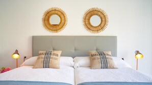 Una cama doble con dos almohadas, cabecera gris y dos espejos redondos fijados a la pared.