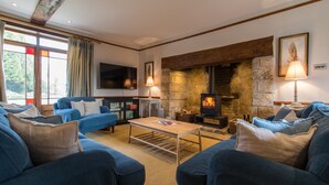 Un salon chaleureux avec une cheminée en pierre, des canapés bleus, un téléviseur à écran plat et une grande fenêtre agrémentée de rideaux.