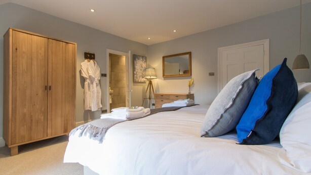 Une chambre à coucher avec un grand lit, une armoire en bois, une salle de bain avec un miroir et une lampe de chevet.