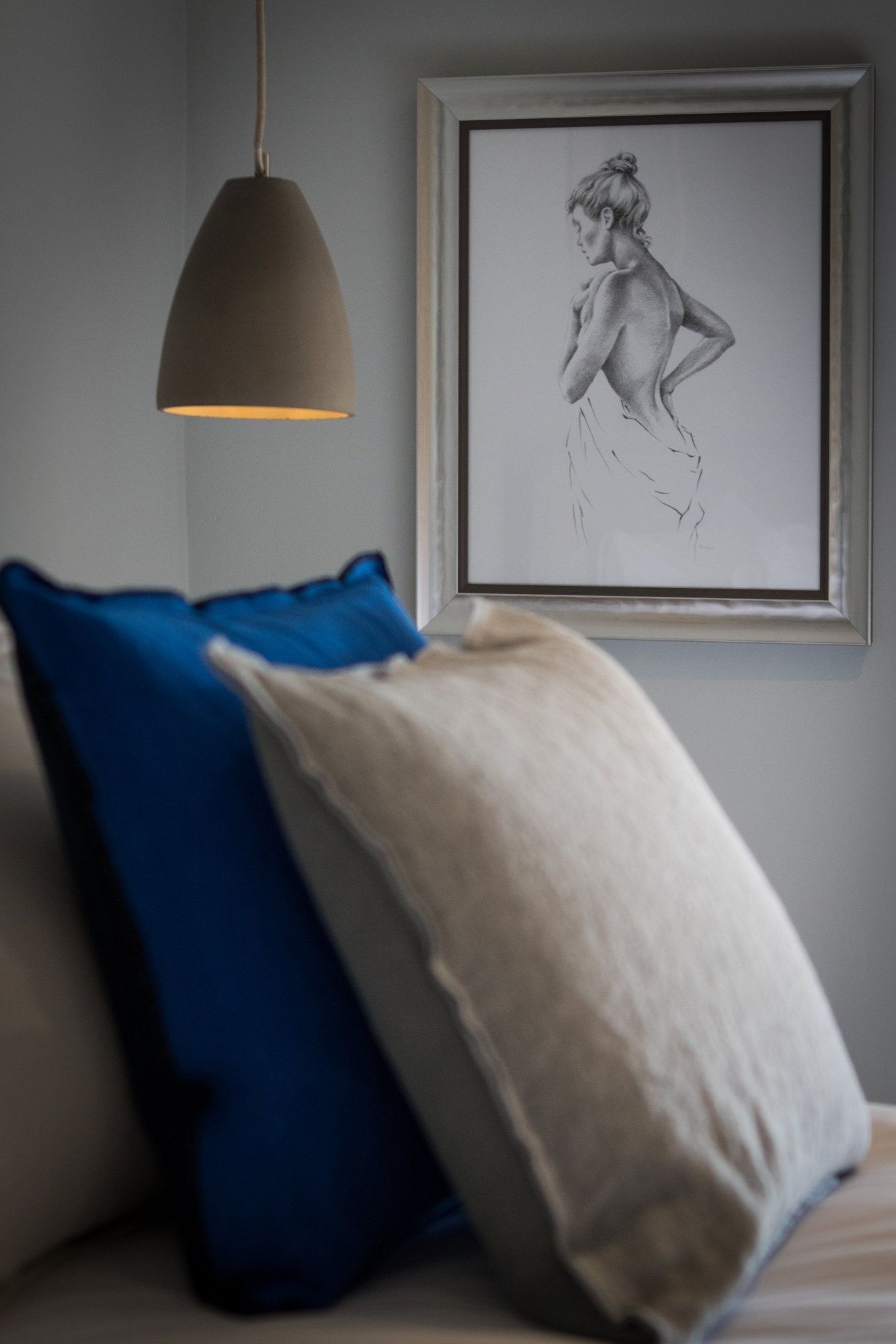 A bedroom with a bed, a blue pillow, a white pillow, and a framed drawing on the wall.