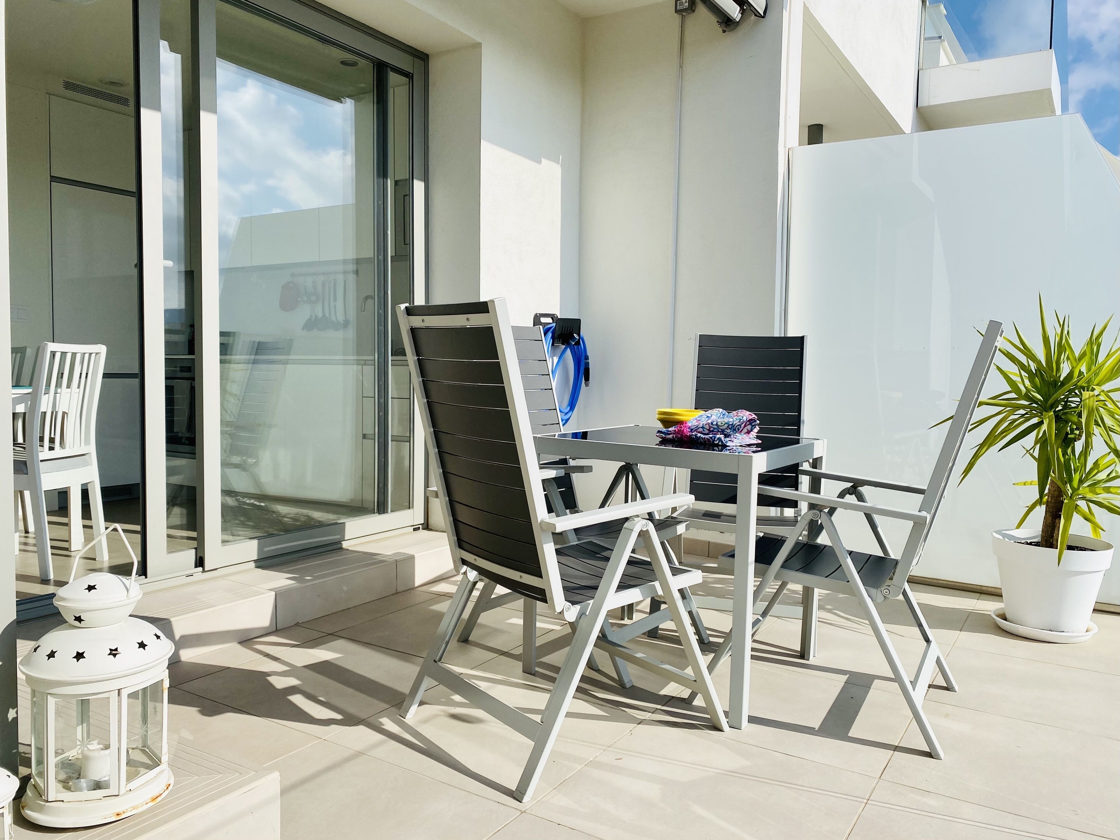 Een balkon met een tafel, stoelen, een bloempot en een lantaarn.