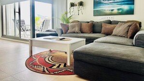 Een moderne woonkamer met een grijze bank, een witte salontafel en een kamerkleed met patroon.
