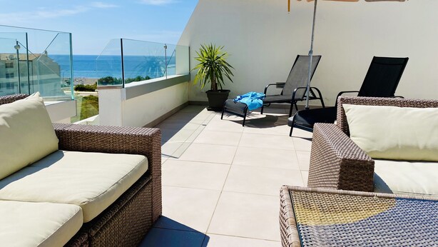 Een balkon met rieten meubilair, een gele parasol en uitzicht op zee.