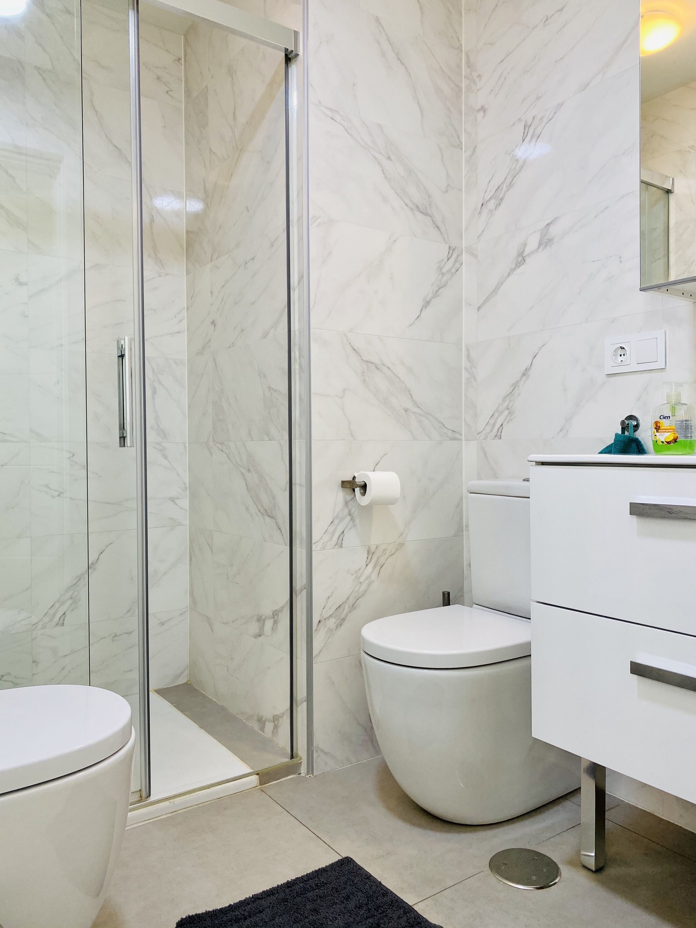 Une salle de bain avec une douche à parois de verre, des toilettes et un meuble-lavabo blanc avec des tiroirs.