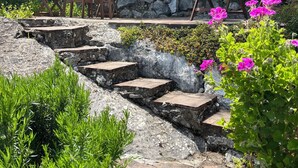 Eine Steintreppe führt zu einer Sitzgelegenheit mit Holzmöbeln und einer Steinwand im Hintergrund.