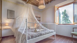 A bedroom with a four-poster bed, a window with a view of trees, and a lamp on a bedside table. - Tognazzi Holiday House - Casa Giglio - Medieval village of Certaldo Alto (Certaldo)