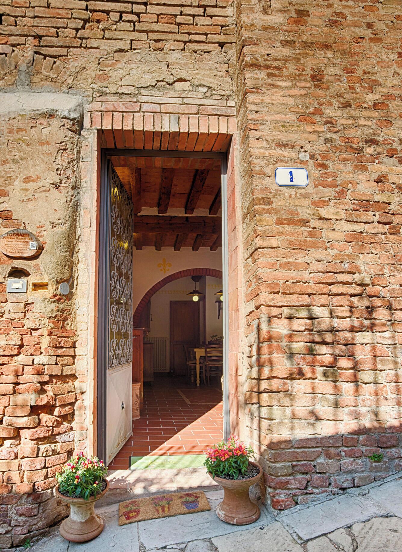 Ingresso di un edificio rustico con facciata in mattoni, una porta in legno e una targa con il numero civico.