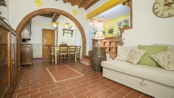 Un interno rustico con zona pranzo, divano e cucina visibile attraverso un arco.