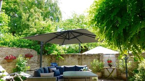 An outdoor seating area with a sofa and a table, a large umbrella, and a stone wall with flowers. - Studio Havenzicht on top location in the historic town of Veere (Veere)