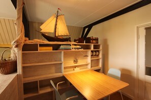 Een kamer met een houten tafel, een stoel, een boekenkast en een klein modelzeilboot.