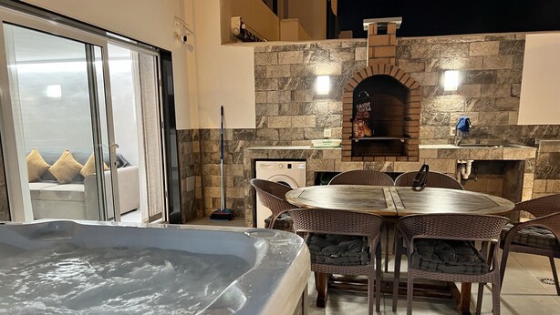 Une terrasse extérieure dotée d’un jacuzzi, d’une cheminée en pierre et d’un coin repas avec des chaises en osier.