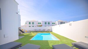 Un espace piscine aménagé sur le toit, avec une pelouse artificielle, des chaises longues et une vue sur les bâtiments blancs qui se dressent à l’arrière-plan.