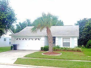 A single-story house with a garage, a small lawn, and a palm tree.