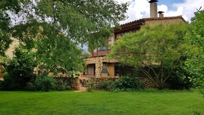 A stone house with a chimney, surrounded by lush greenery and a well-maintained lawn. - Rural house for exclusive rental in Girona (Cabanelles)