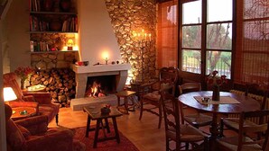 A cozy living room with a fireplace, stone wall, and large windows. - Rural house for exclusive rental in Girona (Cabanelles)