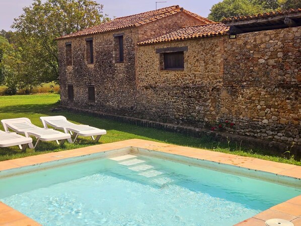 A stone building with a tiled roof, a swimming pool with lounge chairs, and a grassy area. - Rural house for exclusive rental in Girona (Cabanelles)